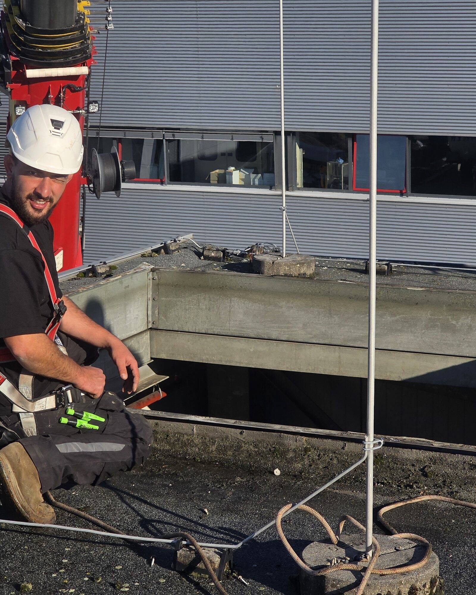 Dachdecker mit Helm und Auffanggurt an einer gespannten Sicherungsleine auf dem Flachdach