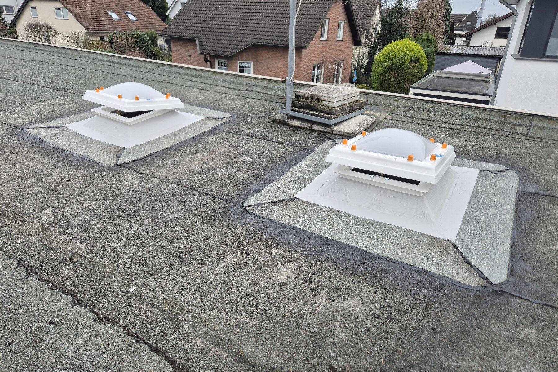 Flachdach mit zwei Lichtkuppeln vor einem Wohngebiet