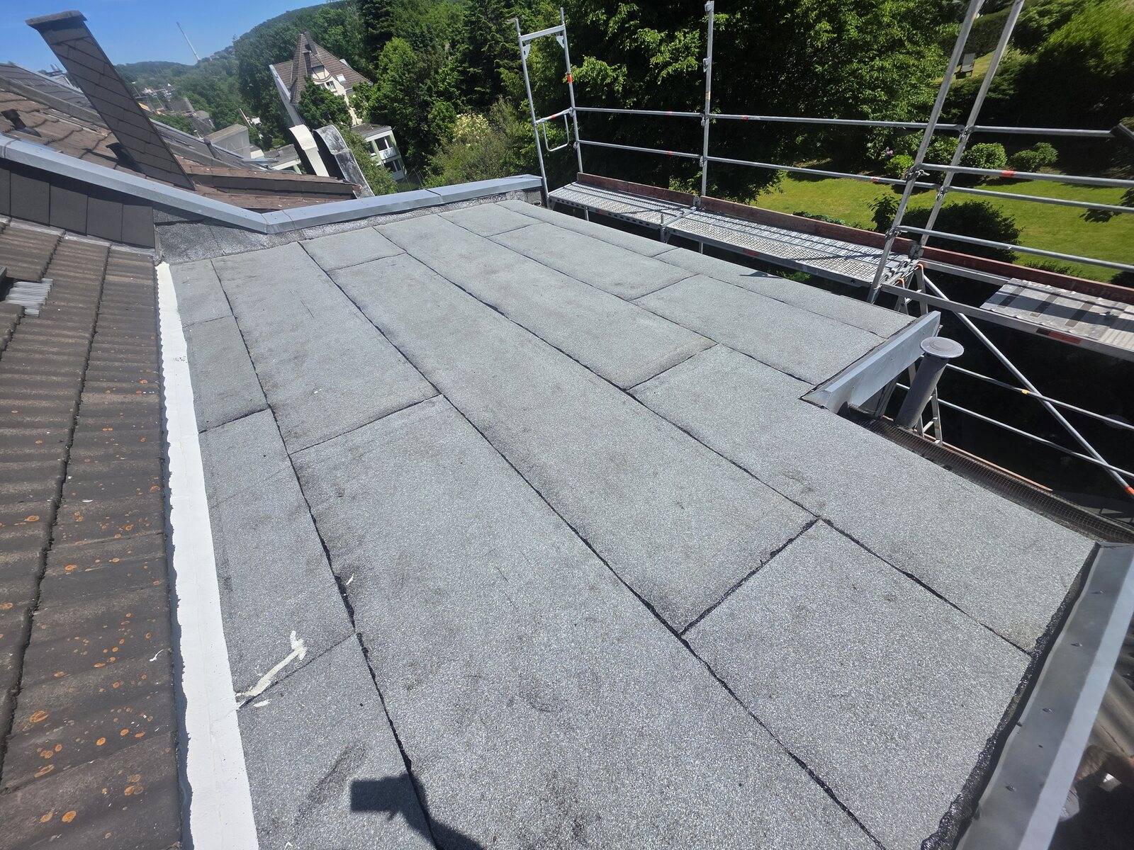 Flachdach mit Bitumenbahnen, Randabschluss und Gerüst im Hintergrund